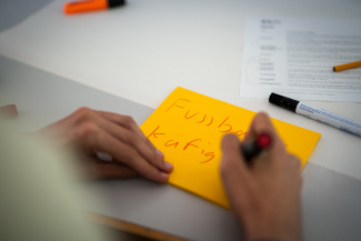 Jemand schreibt auf ein gelbes Post-It: Fussball-Käfig